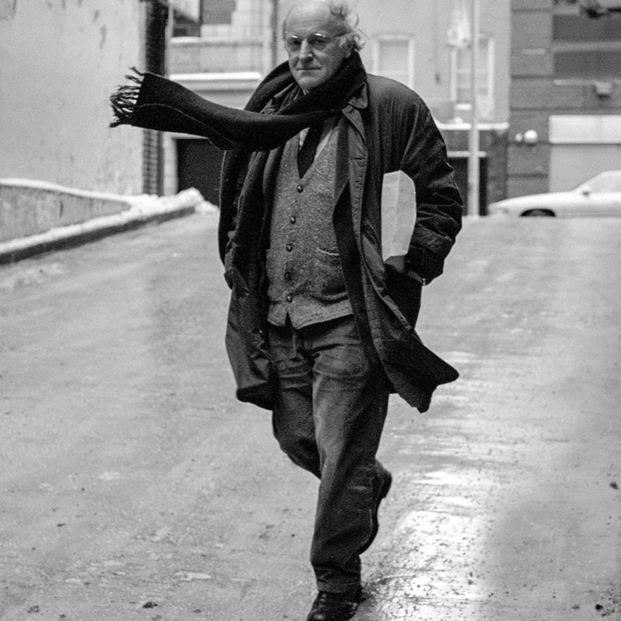 Фото: На вертикальной фотографии изображён Иосиф Бродский в полный рост. Он идёт по улице в расстёгнутом пальто, его шарф развевается на ветру. Его взгляд обращён в камеру.