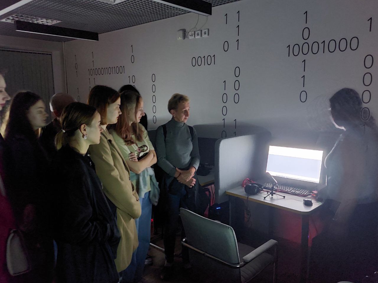 Горизонтальная фотография, на которой сотрудник библиотеки в технохабе (компьютерном классе) рассказывает демонстрирует участникам тифлотехнические устройства и оборудование для записи подкастов
