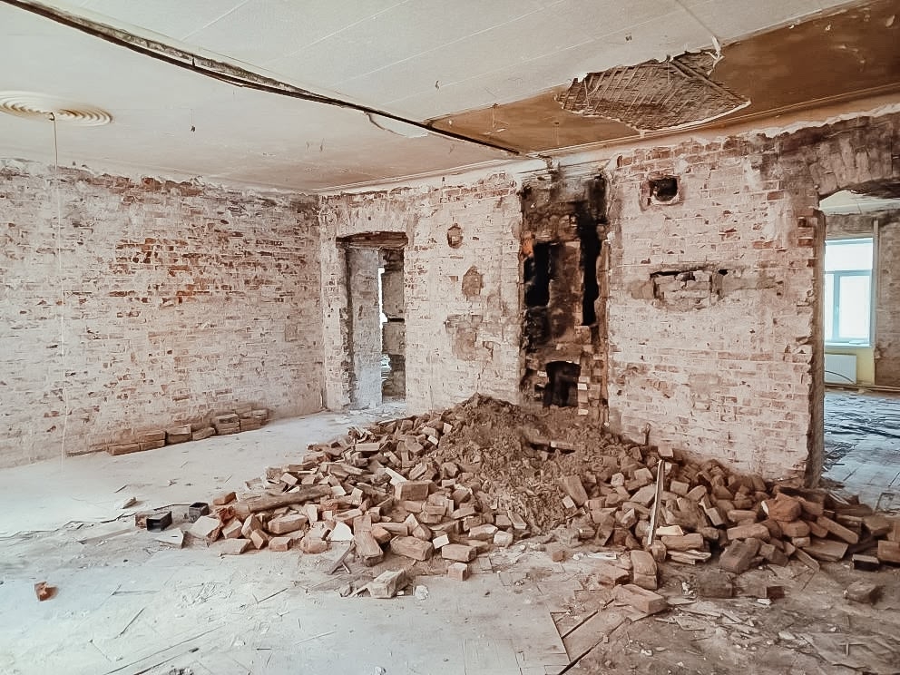 Временное состояние библиотеки во время ремонта: укрытые пленкой стеллажи и кирпичные стены со снятой штукатуркой