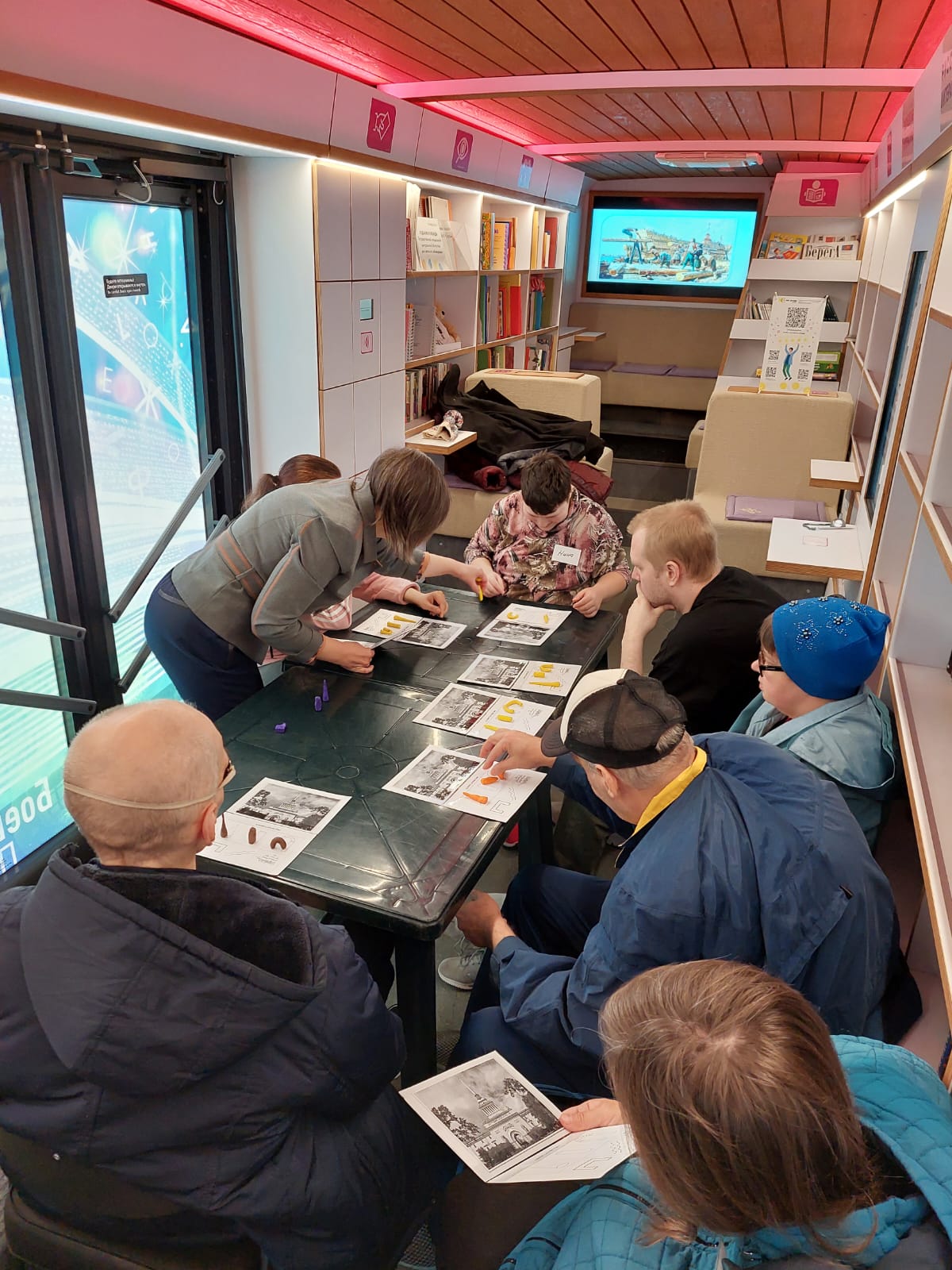 На вертикальной фотографии запечатлён момент проведения мастер-класса. Участники работают с пластилином на мнемокарточках. Им помогает ведущая мероприятия.